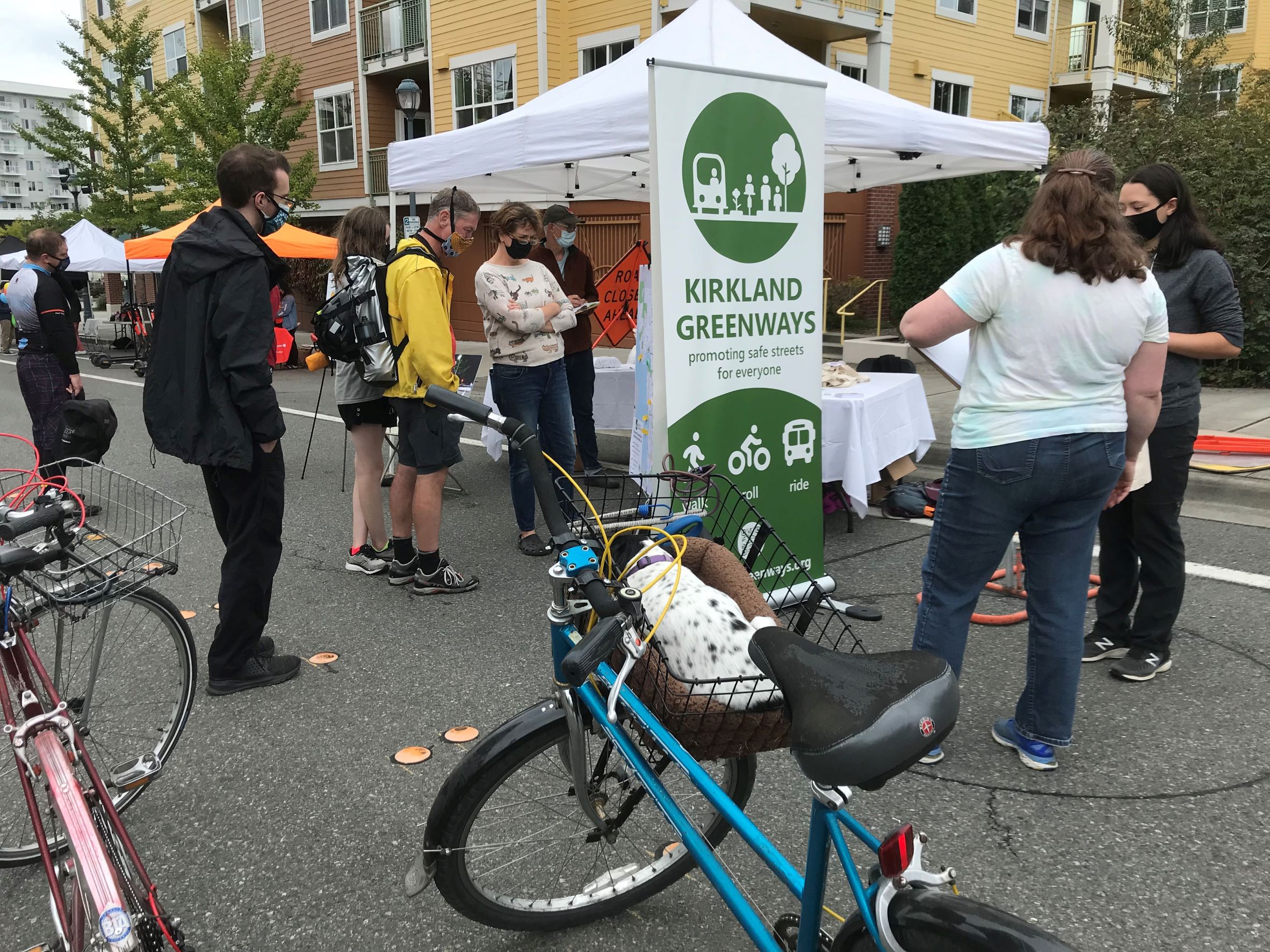 White tent booth space with Kirkland Greenways group, People engaging with the booth and bike with a dog in the basket in front.